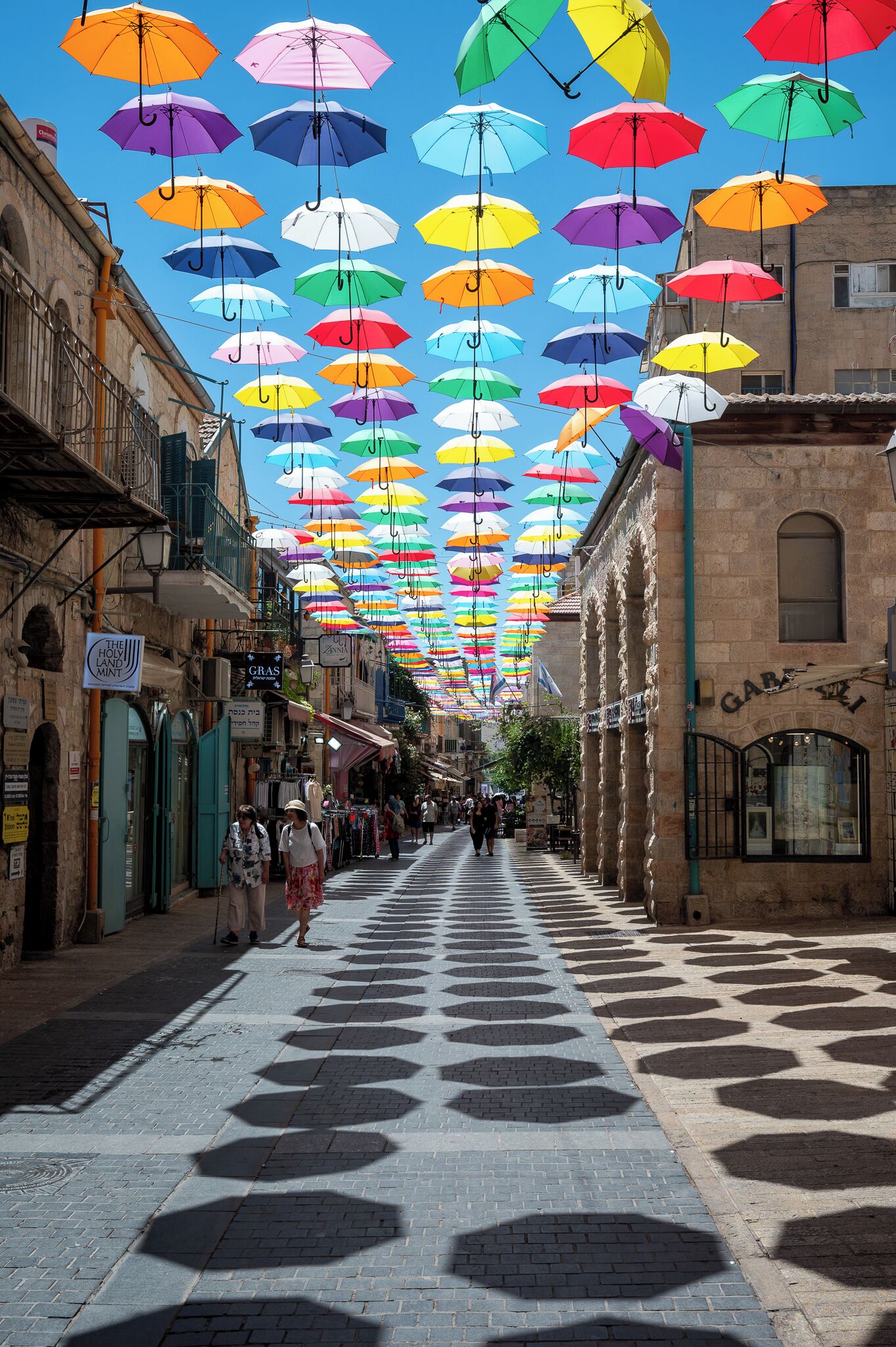 A street with a pattern of hexagonal tiles on the ground and colorful umbrellas hanging overhead.