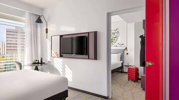 Une chambre d’hôtel avec un lit, un téléviseur fixé au mur, une petite table avec une lampe et une vue sur la ville par la fenêtre.