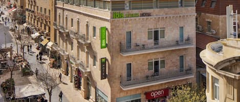 A hotel with a green sign, multiple balconies, and a storefront with a red sign.