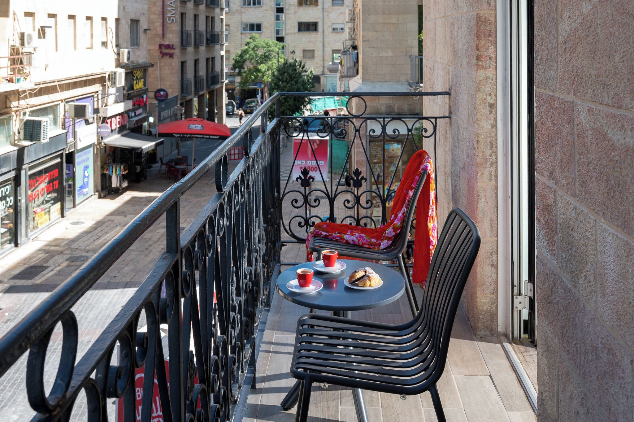 A balcony with a table and chairs, a red chair, and a red umbrella.