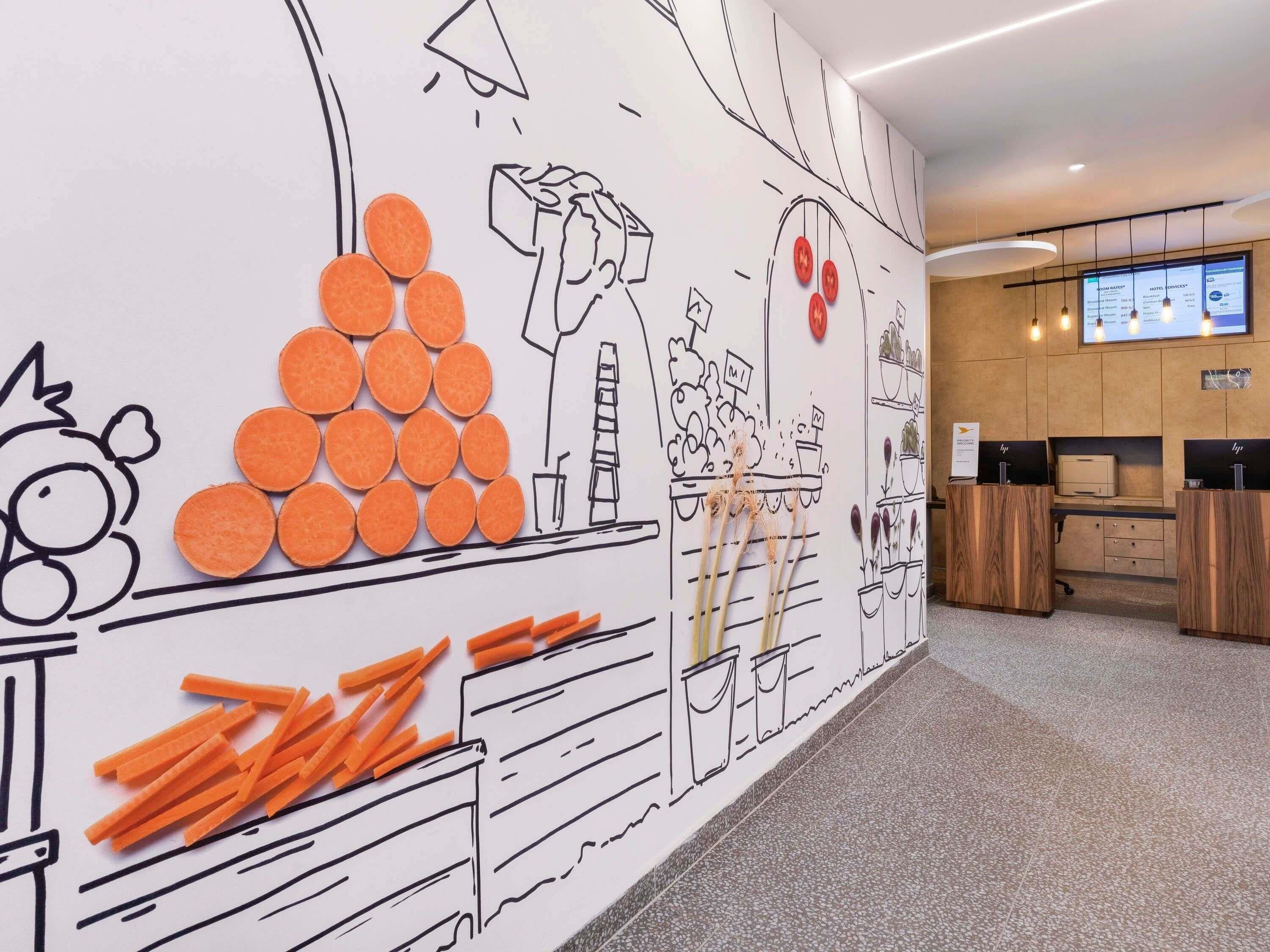 Eine Hotellobby mit Wandgemälde, einer Rezeption und einem digitalen Bildschirm, der Zimmerpreise anzeigt.