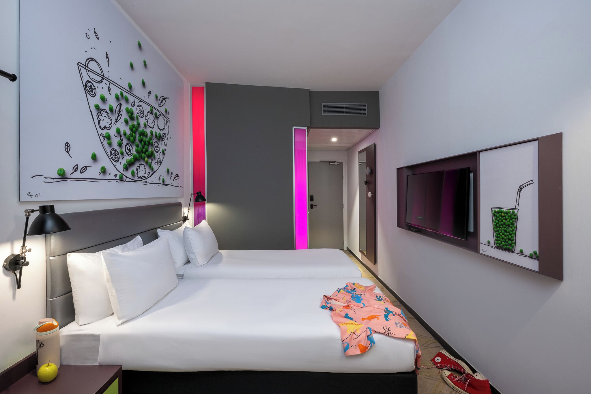 Una habitación de hotel con cama, mesita de noche, lámpara, una obra de arte en la pared, televisor y puerta con luz rosa.