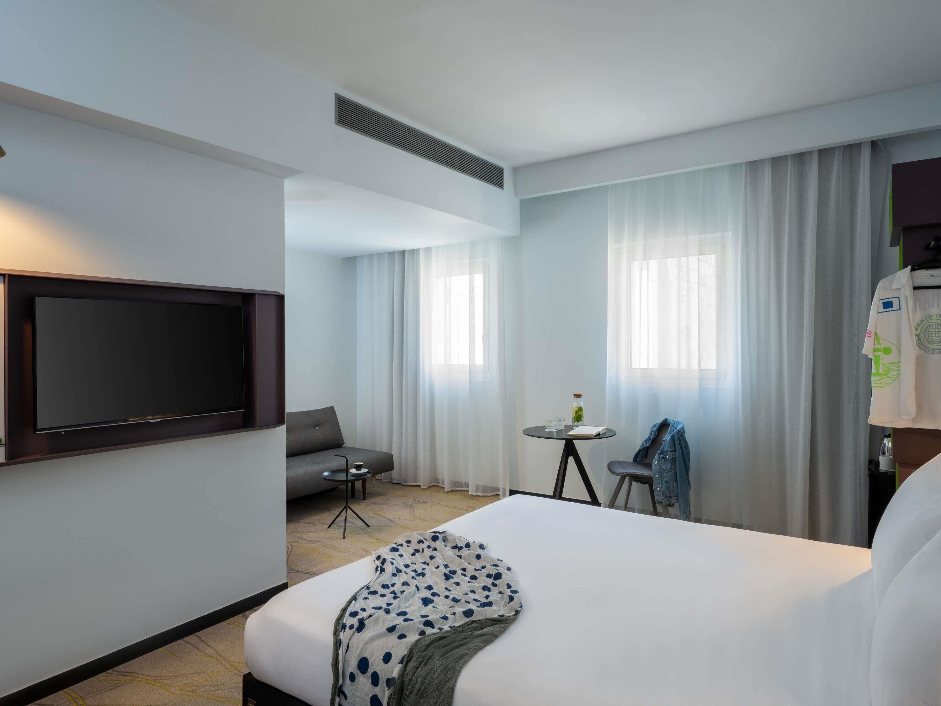 Habitación de hotel con cama, televisor, una mesita con silla y un escritorio con silla.