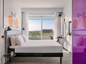 A hotel room with a bed, a desk, a chair, a window with a city view, and artwork on the walls. - ibis Styles Jerusalem City Center - An AccorHotels Brand (Jerusalem)