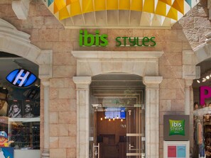 A hotel entrance with 'ibis styles' signage, a visible reception desk, and a glass door.