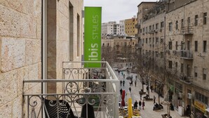 A building with a stone facade, a balcony with wrought iron railings, and a street below with people walking and outdoor seating. - ibis Styles Jerusalem City Center - An AccorHotels Brand (Jerusalem)