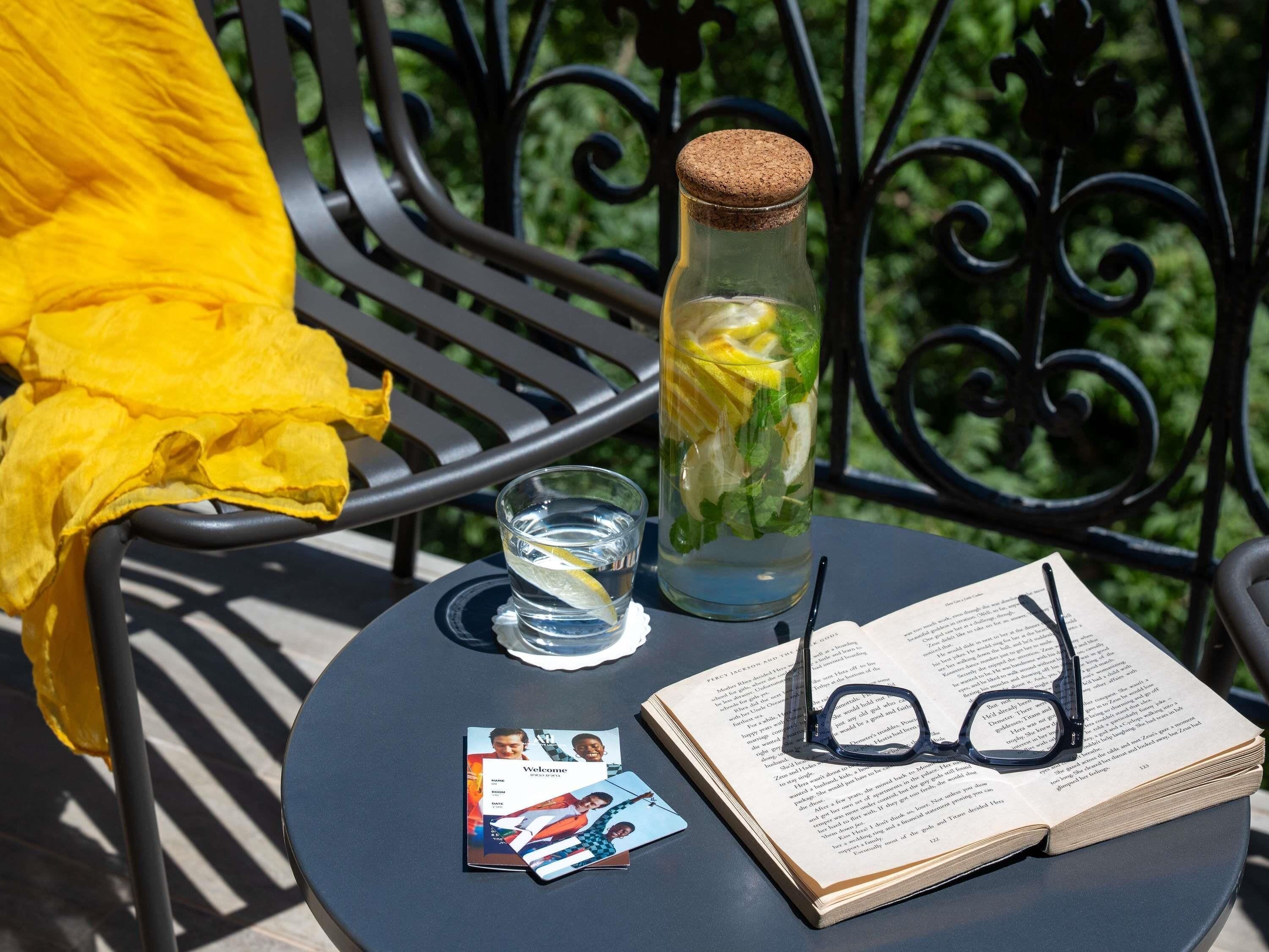 A table with a book, a pair of glasses, a glass of water, and a bottle with a cork.