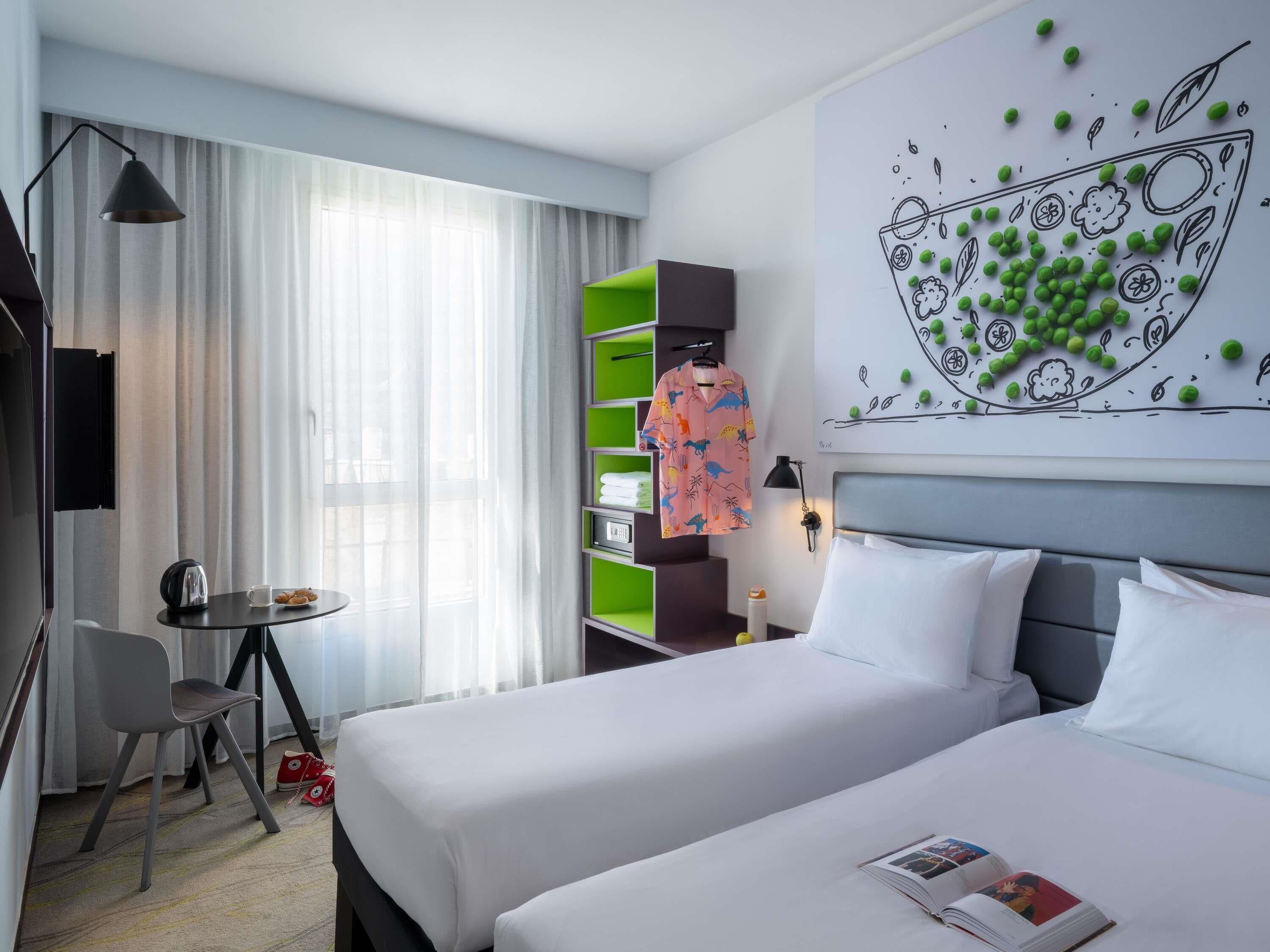 Habitación de hotel con dos camas, un escritorio, una silla, una lámpara y una obra de arte en la pared.