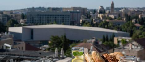 Una mesa con pasteles, una bebida y una caja de madera con la etiqueta 'WOOD BOX' en un balcón con vistas a la ciudad.