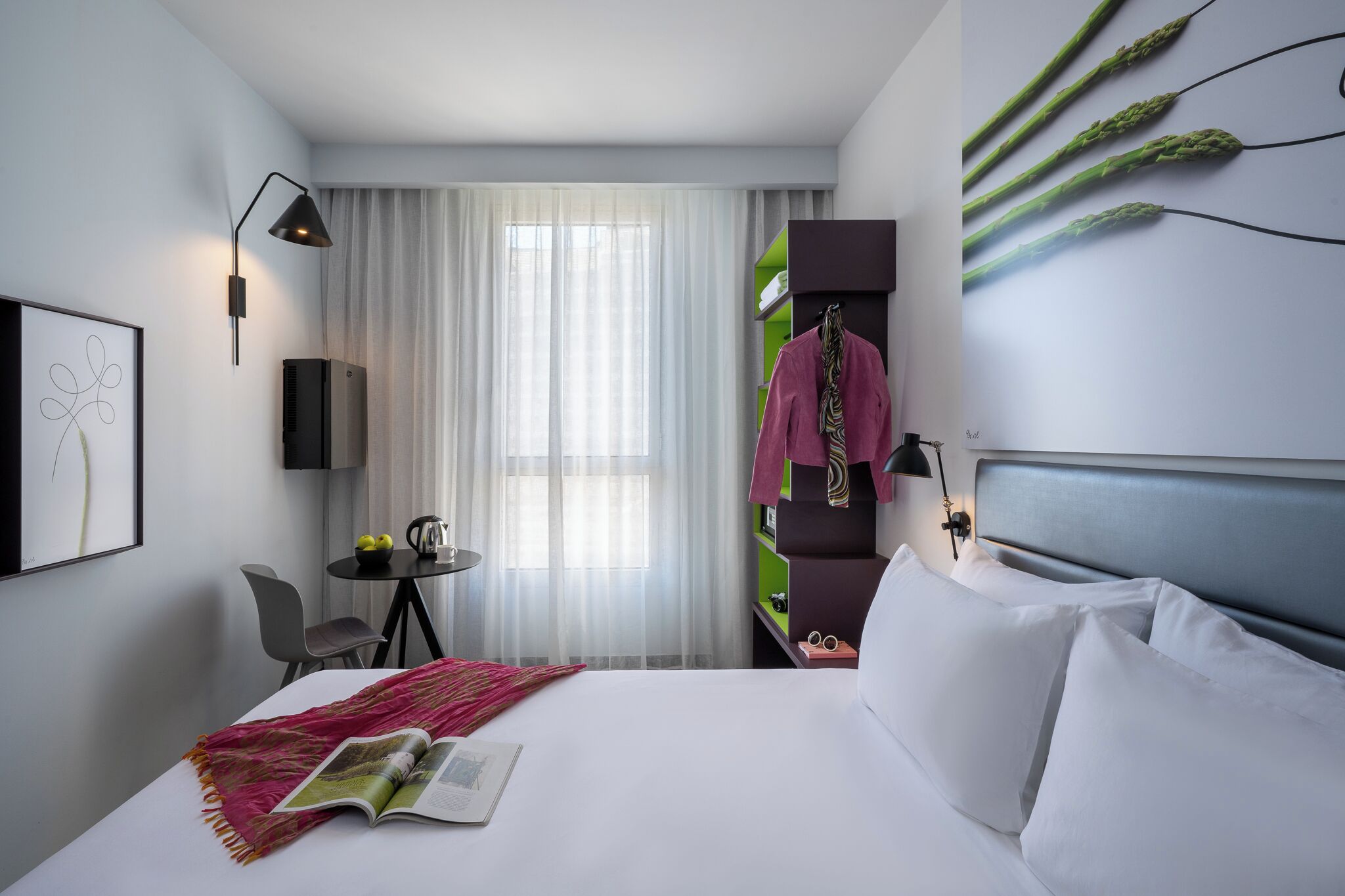 Een moderne hotelkamer met een bed, een bureau, een stoel, een klein tafeltje met een waterkoker, en een tv aan de muur.