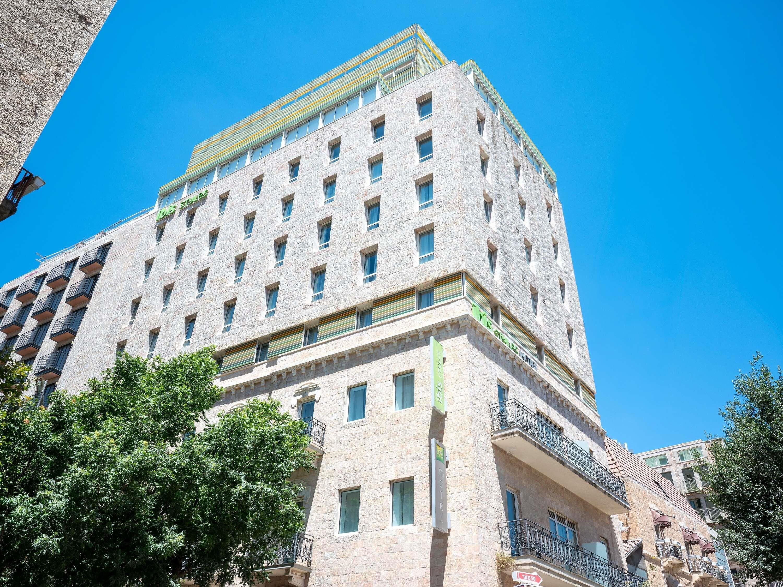 A multi-story hotel with a stone facade, balconies, and a clear blue sky.