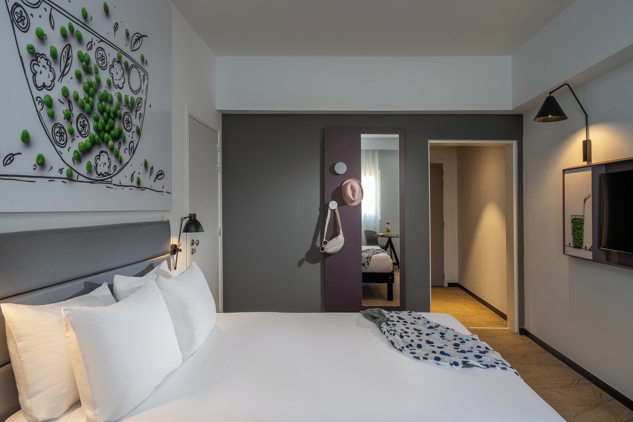 A modern hotel room with a large bed, a desk, a chair, a mirror, and a television.