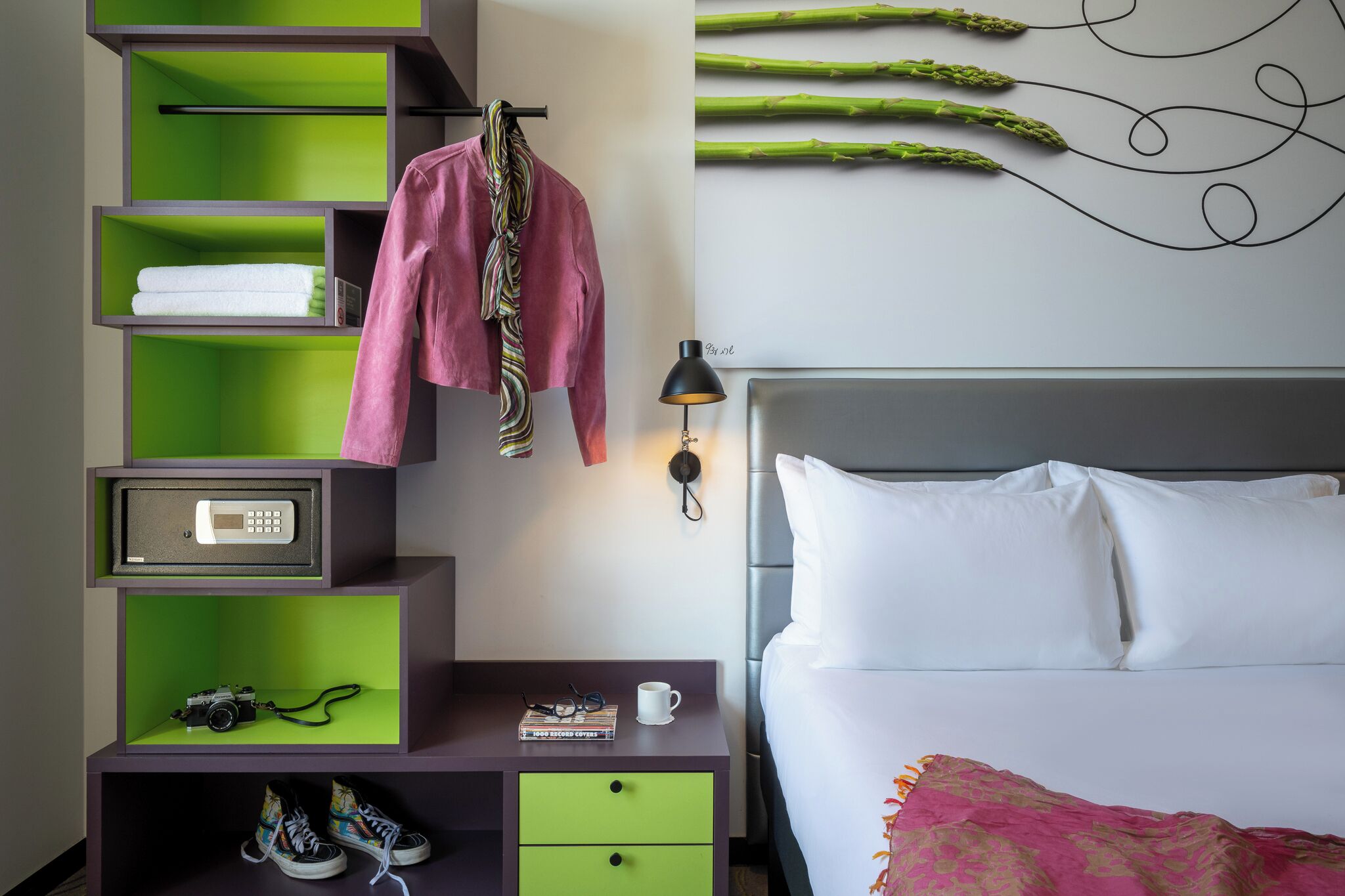 Un dormitorio con una cama, una mesita de noche, un estante verde y una lámpara de pared.