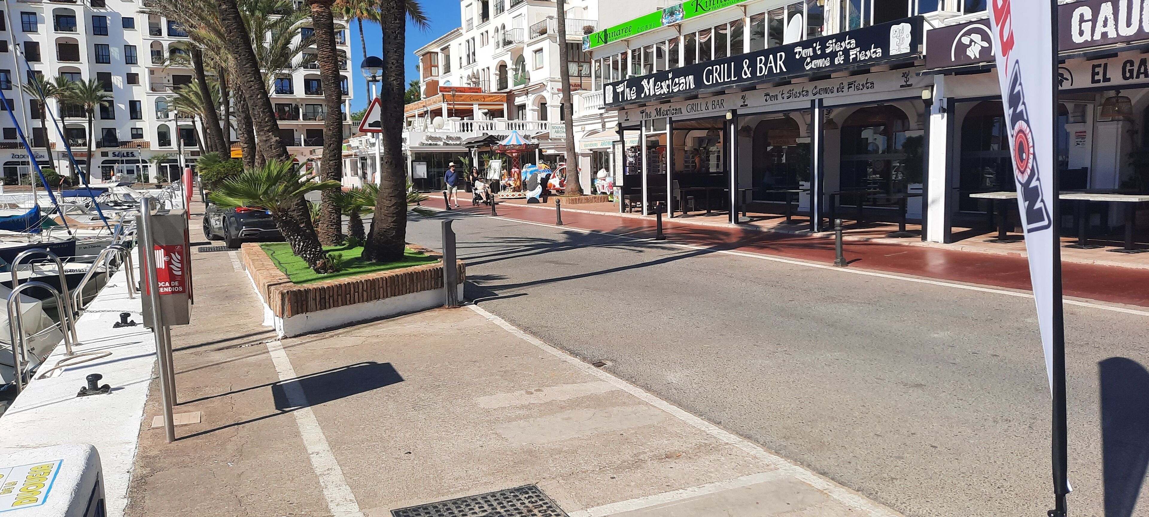 Une vue de rue avec un restaurant-bar mexicain, des palmiers et des voitures garées.