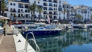 Una marina con barcos amarrados, un edificio blanco con balcones y palmeras.