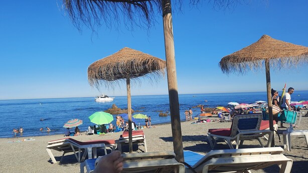 Una playa con sombrillas de paja, sillas de descanso y un bote en el agua.