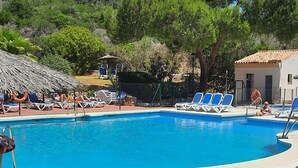 Una piscina con sillas de descanso y una mesa, rodeada de follaje y colinas.