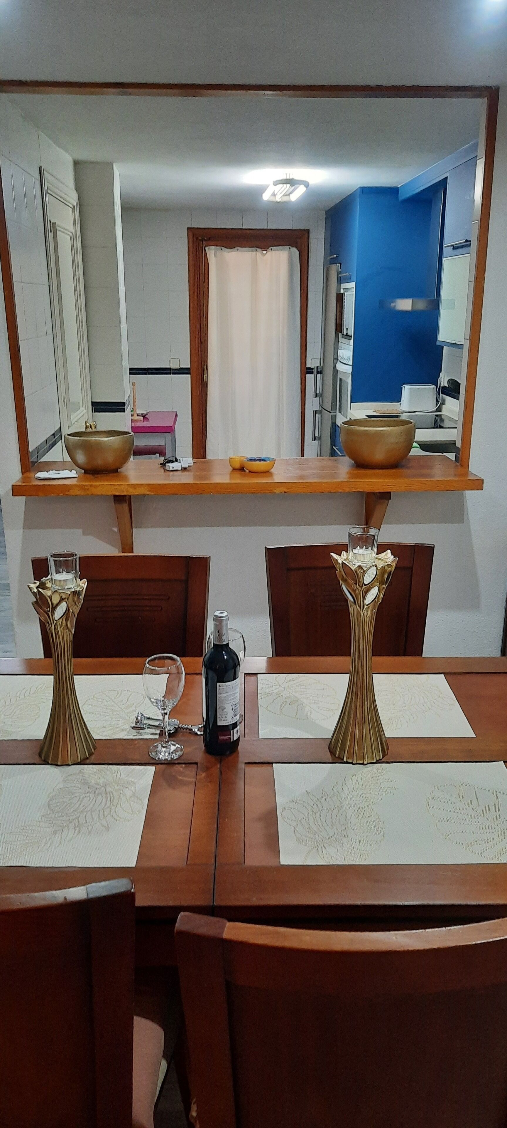 Un coin repas avec une table en bois, des chaises et deux vases décoratifs. Une bouteille de vin et un verre sont posés sur la table.