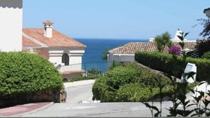 Una calle costera con edificios, cielo azul despejado y el mar al fondo.