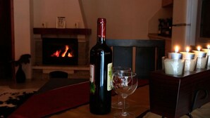 Eine Weinflasche und ein Glas auf einem Tisch mit angezündeten Kerzen in einem gemütlichen Raum mit Kamin.