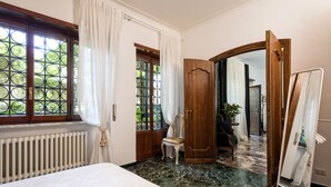 Une chambre à coucher avec un lit, un radiateur, une fenêtre avec des rideaux, une porte en bois et un miroir.