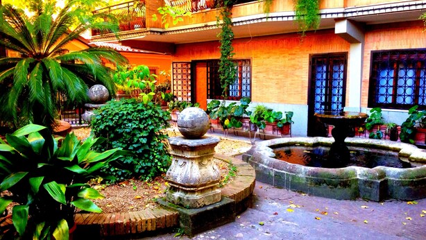 Une cour avec une fontaine, des plantes en pot et un bâtiment doté d’un balcon.