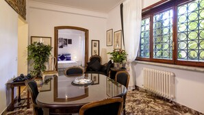 Une salle à manger avec une table ronde, des chaises, une plante en pot et une fenêtre donnant sur un paysage verdoyant.