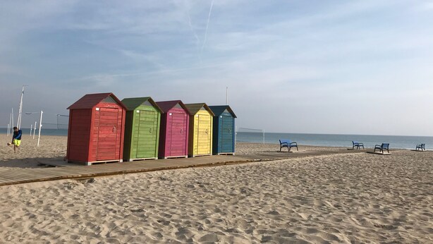 Une plage avec des cabanes de plage aux couleurs vives et une promenade en bois.