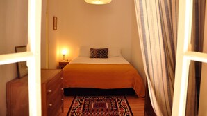 A bedroom with a bed, a bedside lamp, a wooden dresser, and a patterned rug. - Comfortable and stylish apartment, fully equipped, in Lapa in Lisbon (Lisboa ciudad)