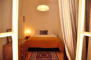 A bedroom with a bed, a bedside lamp, a wooden dresser, and a patterned rug.