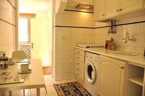 Eine kleine, saubere Küche mit Waschmaschine, Spüle und einem Fenster mit Jalousien.