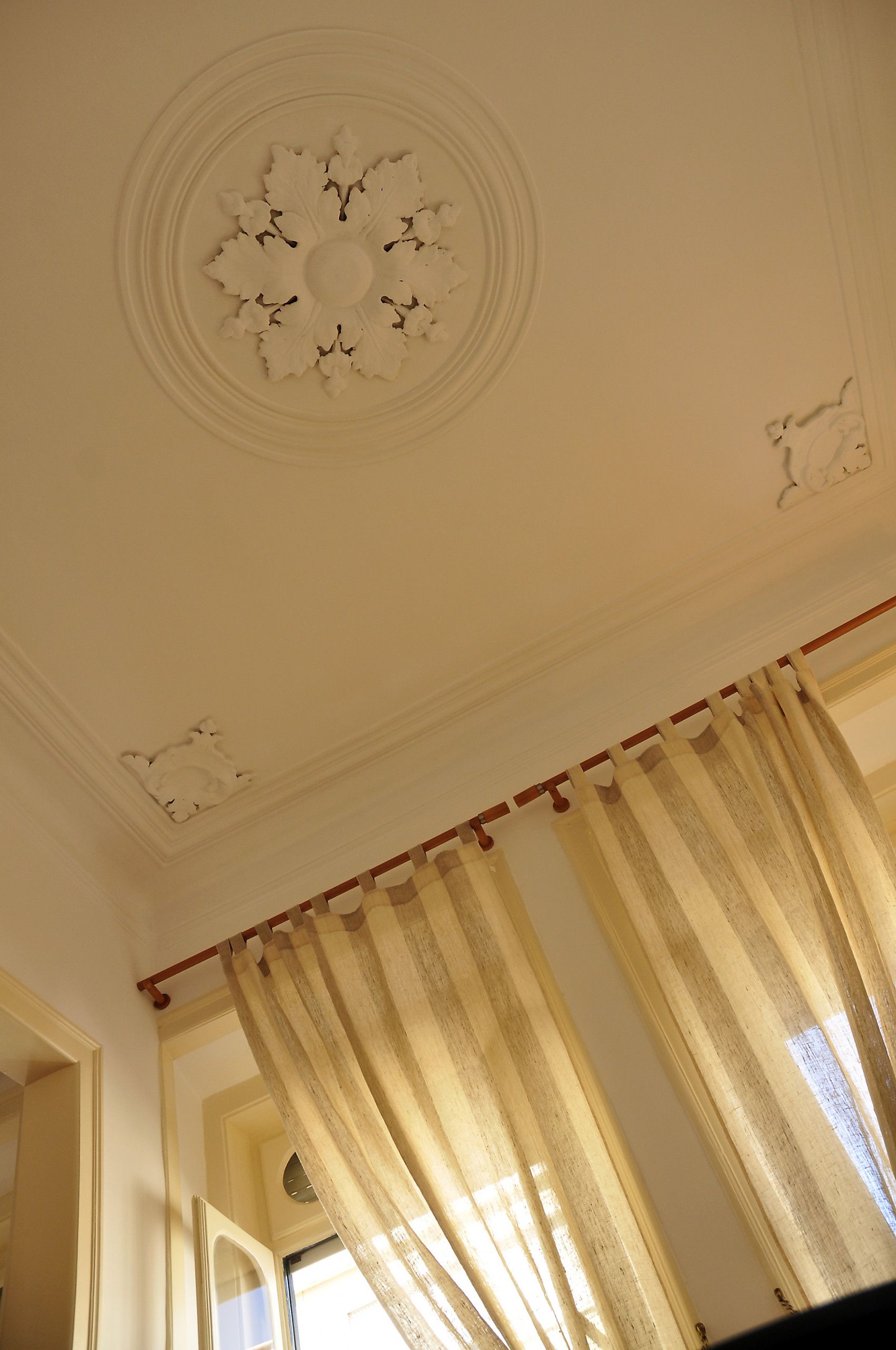 Una stanza con soffitto decorato, una finestra con tende e una porta che dà su un'altra stanza.
