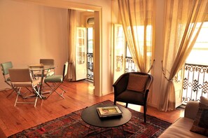 A living room with a glass table, two chairs, a sofa, and a patterned rug.