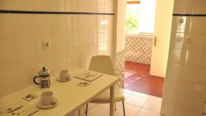 A small dining area with a white table, a chair, and a coffee maker. There is a window with blinds and a door leading to another room. - Comfortable and stylish apartment, fully equipped, in Lapa in Lisbon (Lisboa ciudad)