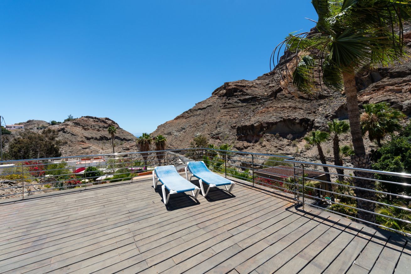 Eine Terrasse mit zwei Liegestühlen, einem Geländer und Blick auf felsiges Gelände und Vegetation.