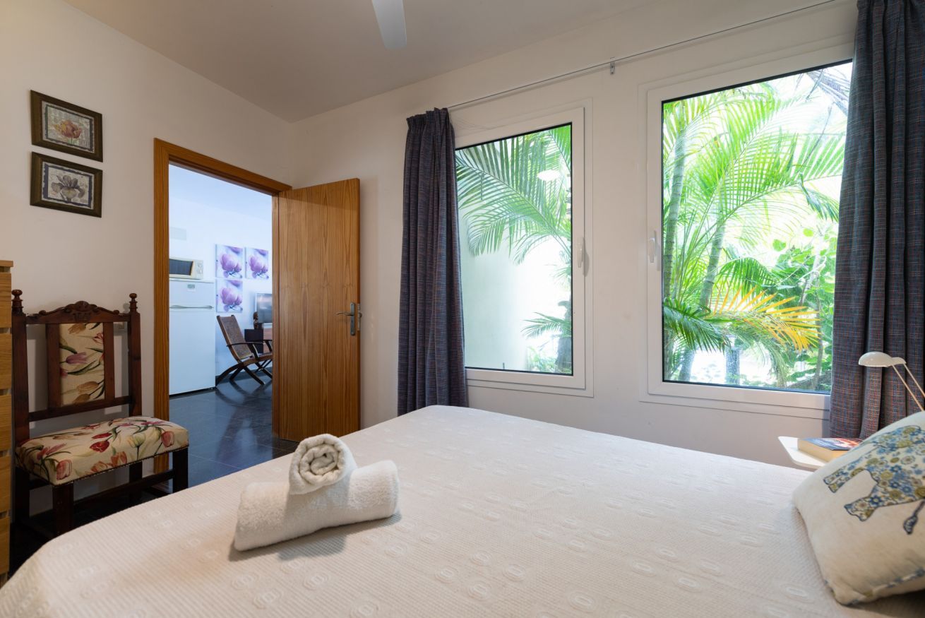 Een hotelkamer met een bed, een stoel, een raam met uitzicht op palmbomen en een deur naar een badkamer.