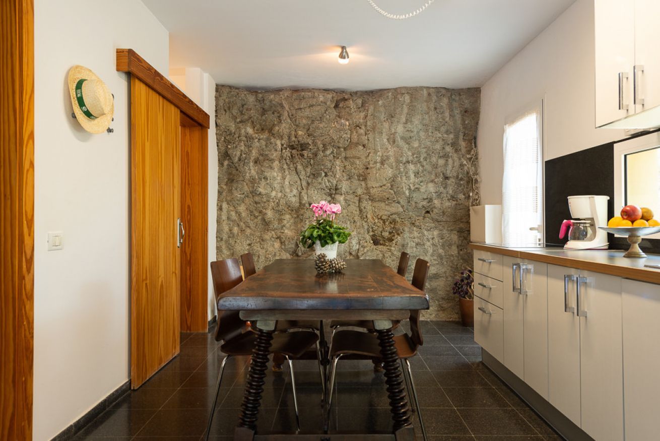 Une cuisine moderne avec un mur d’accent en pierre, des armoires en bois et une table à manger avec des chaises.