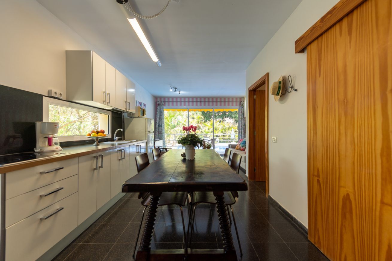 A modern kitchen with a dining table, cabinets, and a view through the window.