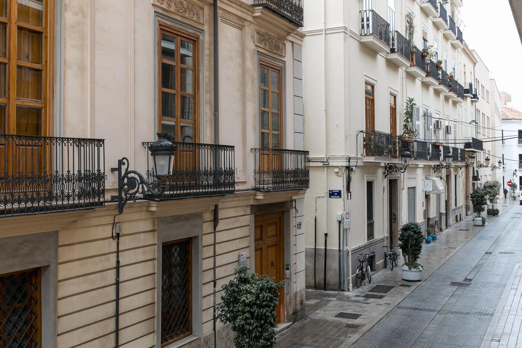 A row of traditional European townhouses with balconies, a cobblestone street, and a clear sky.