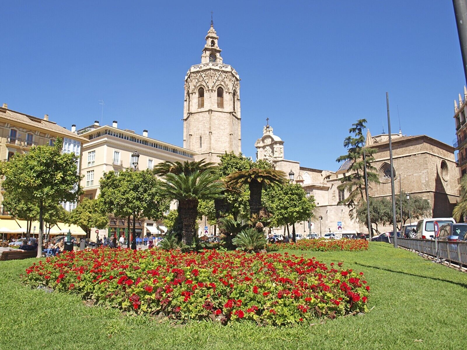 A historic building with a prominent tower and a well-maintained flower garden in front.