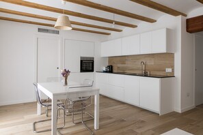 Une cuisine moderne avec des meubles blancs, un plan de travail en bois et un coin repas comprenant une table en verre et des chaises en métal.