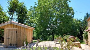 Ein hölzernes Gartenhaus mit Tür und Fenstern, umgeben von einem Garten mit Lavendel und einer Bank.