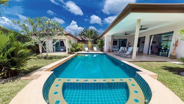 Piscina con jacuzzi integrado, rodeada por un porche cubierto con sillones de descanso y vistas a una casa moderna con amplias ventanas.