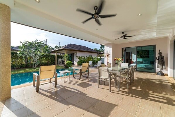 A covered patio with a pool, outdoor seating, ceiling fans, and a statue.