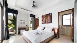 Un dormitorio moderno con una cama grande, un ventilador de techo, un cuadro de Buda y vistas al exterior.
