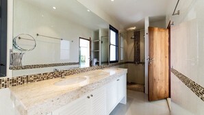 Un baño moderno con un espejo grande, dos lavamanos y una zona de ducha.