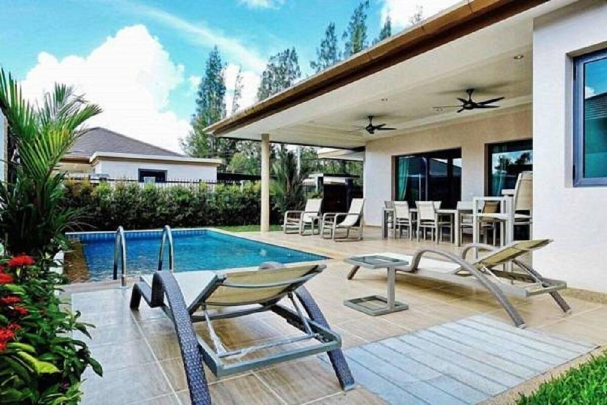 Un espace piscine extérieur moderne, doté de chaises longues et d’un coin salon abrité.