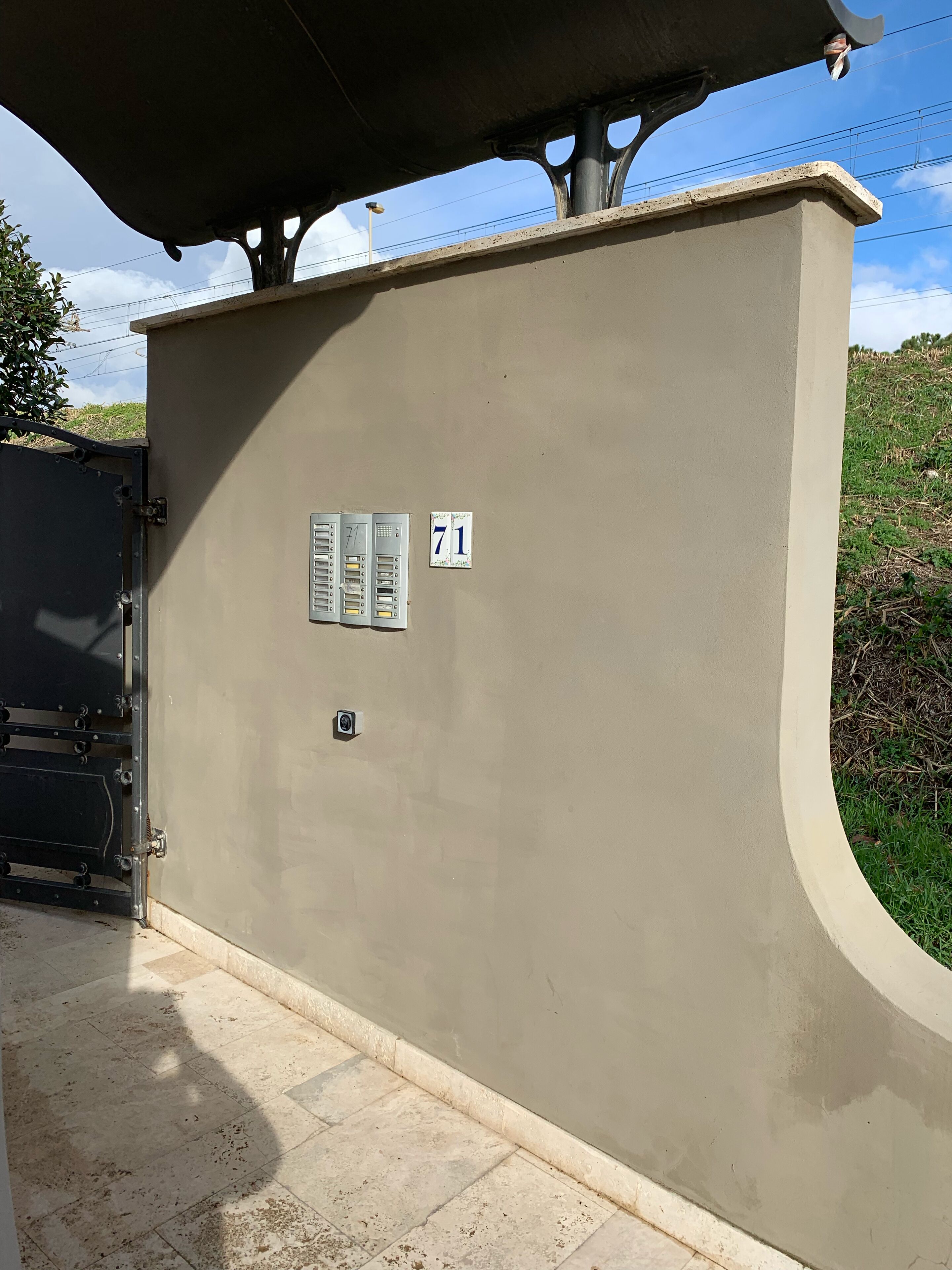 A beige utility box with a number 71 sign, a metal gate, and a concrete structure with a curved top.