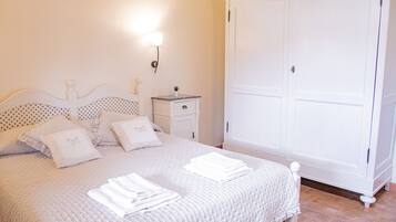 Un lit bien fait, avec une literie et des oreillers blancs, une table de chevet avec une lampe, et une grande armoire blanche.