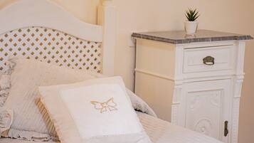 A neatly made bed with a white headboard, a bedside table with a plant, and a drawer.